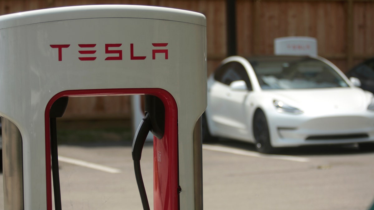 A Tesla supercharging location is seen with a white Tesla in the background.