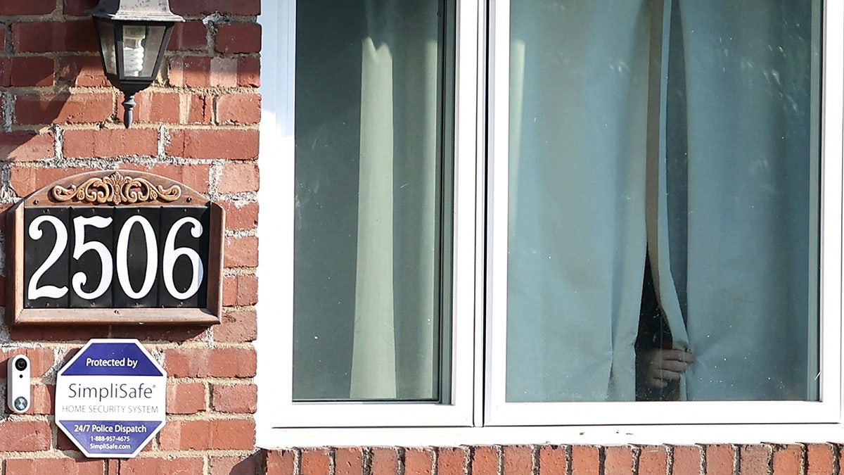 An unknown person adjusts the window shades inside the home of Thomas Matthew Crook