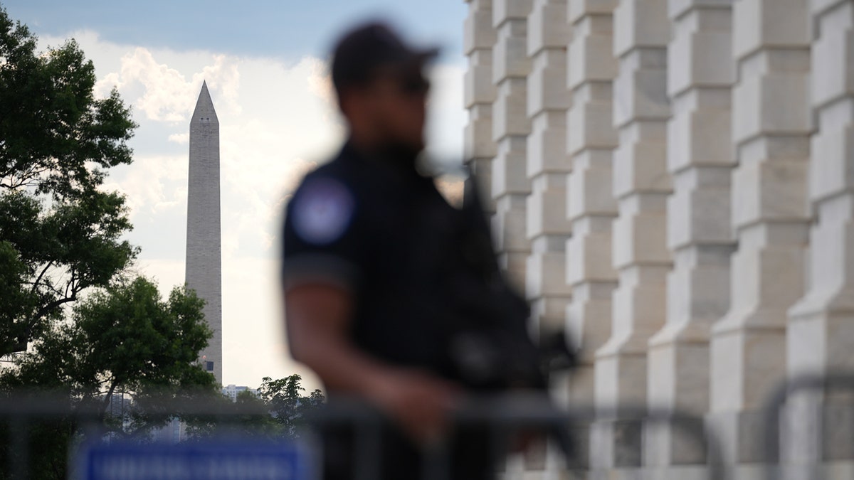 A Capitol Police officer stands guard outside the U.S. Capitol building with the Washington Monument in the background.