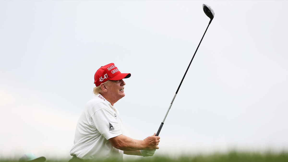 Donald Trump in white shirt and red hat swings a golf club