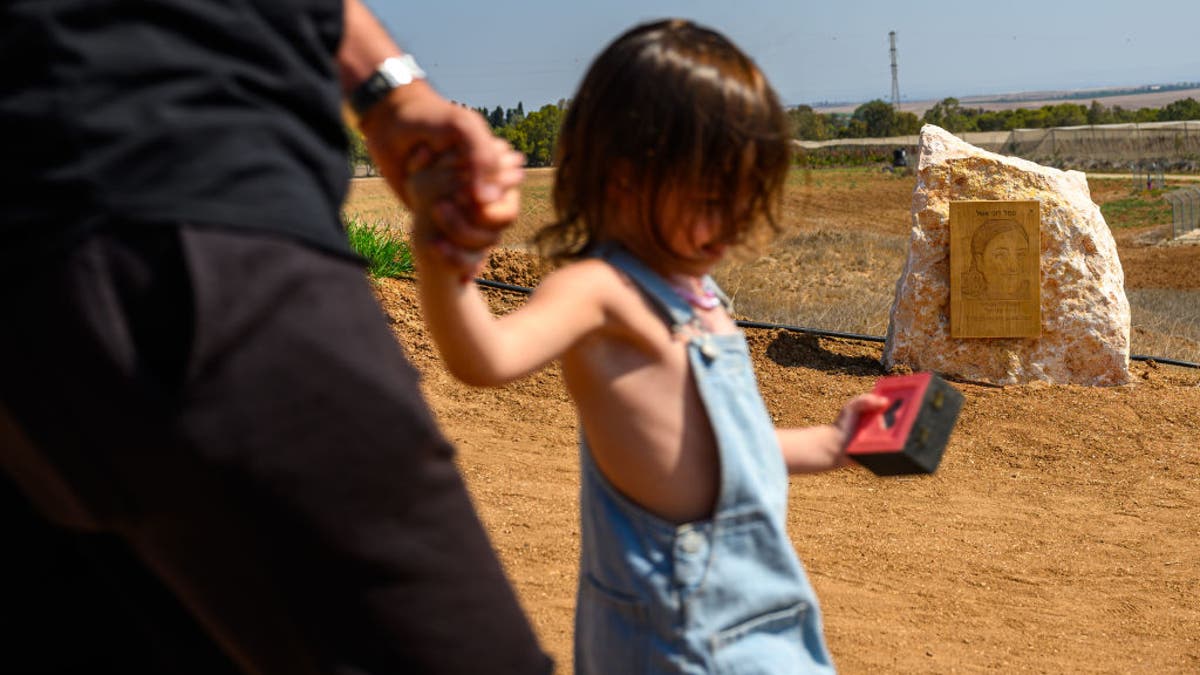 A girl and her father walk past a boulder and photo for the killed soldier Roni Eshel at a new memorial for the surveillance soldiers killed on October 7th during the attack on the Nahal Oz base on October 4, 2024, near Nahal Oz, Israel. On the morning of October 7, the Nahal Oz base was attacked by Hamas terrorists, where 66 soldiers were killed, including 15 female soldiers who operated surveillance cameras. Some of the female soldiers who were not killed were taken hostage on October 7, 2023.