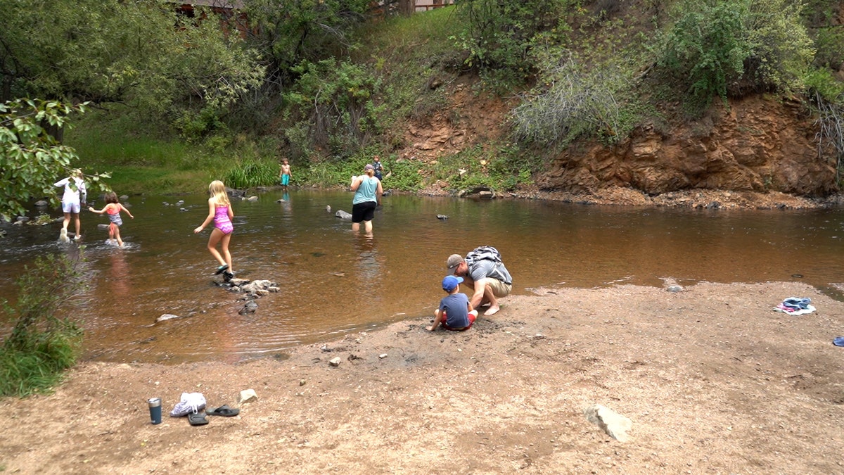 Man, woman and several children play in creek