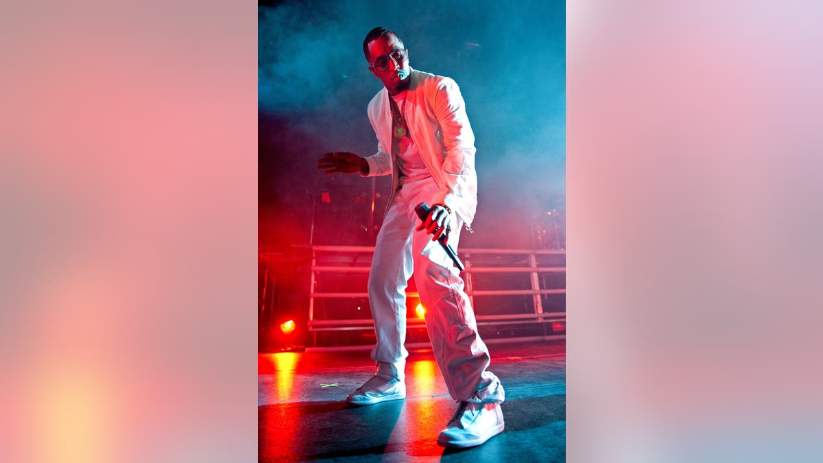 Diddy dances during a performance, wearing all white under red and blue stage lights