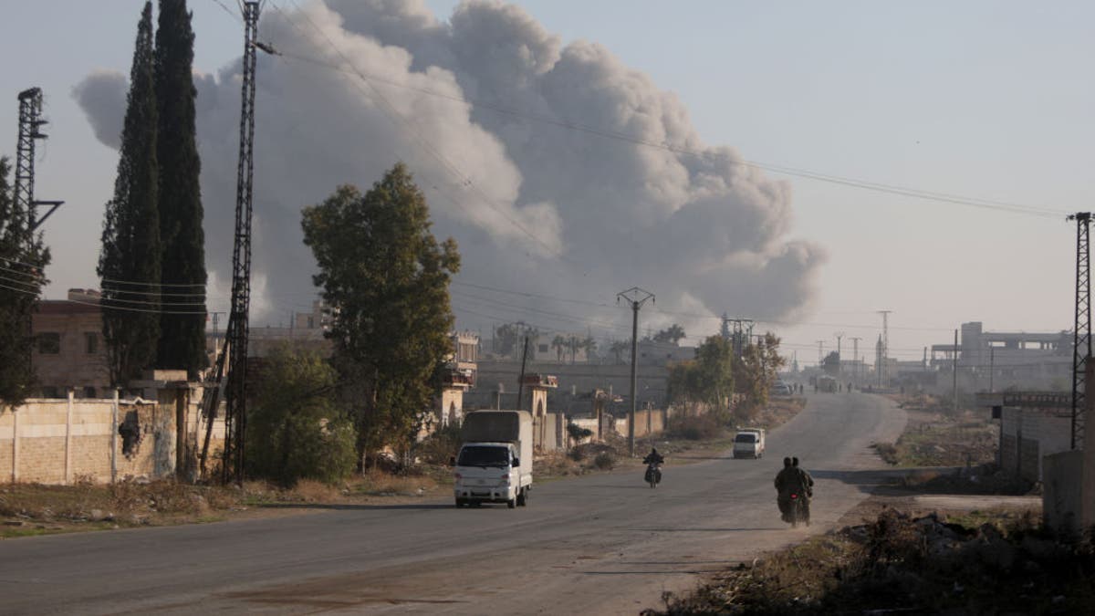 Fighters enter the Rashidin district on the outskirts of Aleppo on their motorbikes with smoke billowing in the background during fighting on November 29, 2024, as Hayat Tahrir al-Sham (HTS) jihadists and allied factions continue their offensive in the Aleppo province against government forces.