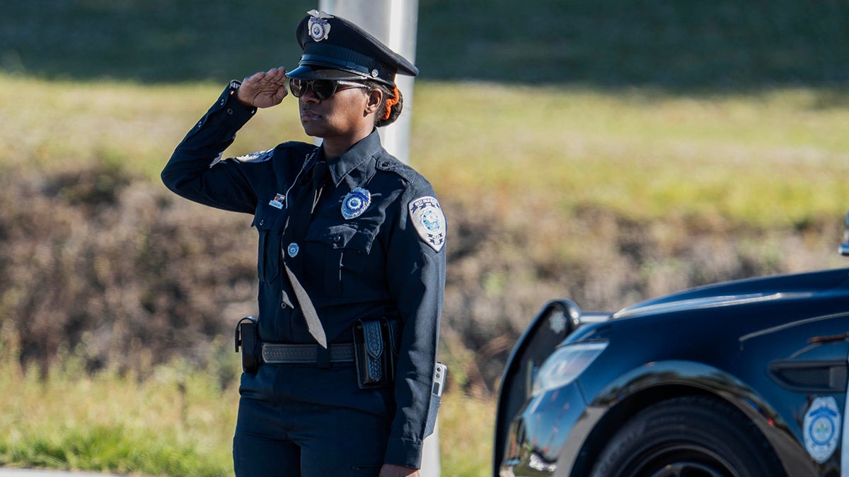 A police officer salutes as a procession for three Palm Beach County Sheriff's Office deputies who died last month