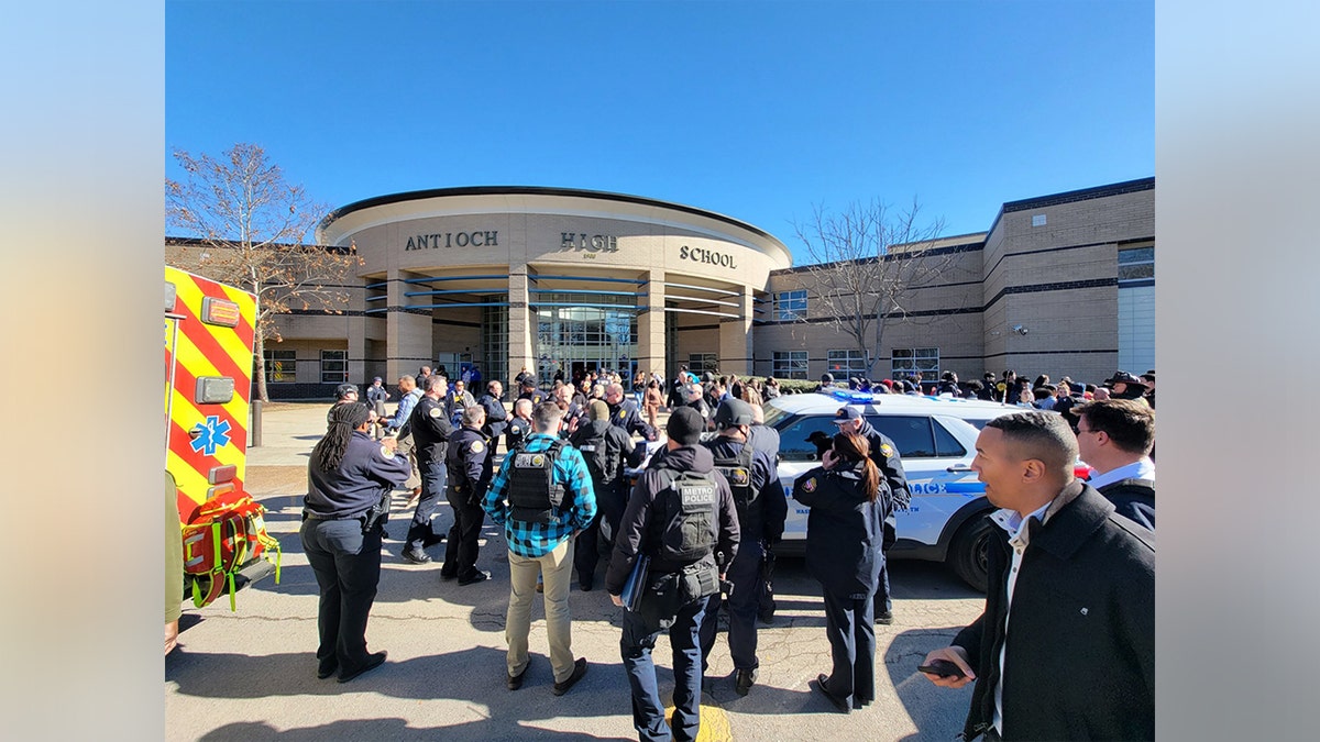 A crowd of civilians and police officers gathers outside of Antioch High School.