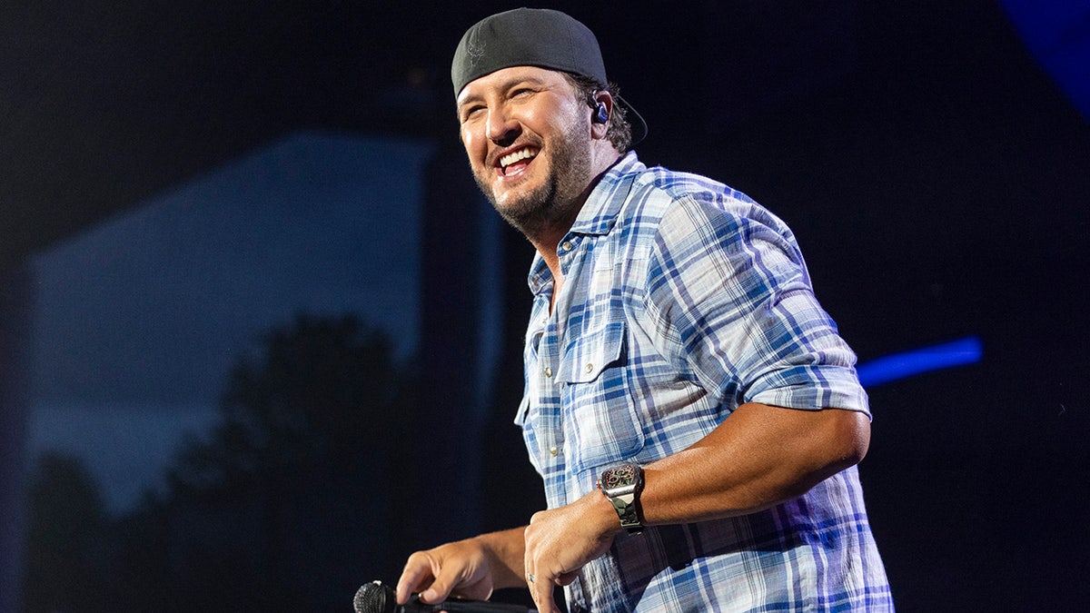 Luke Bryan smiling on stage in a blue flannel