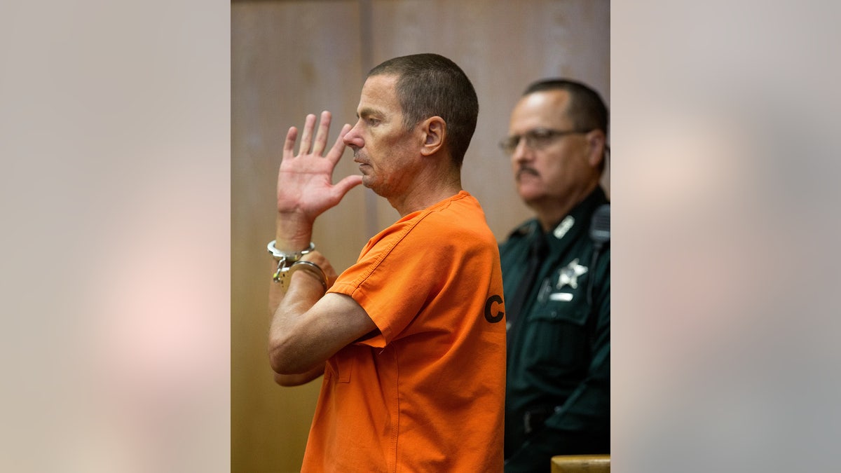 Jeremy Scott raising his hand in an orange jumpsuit.