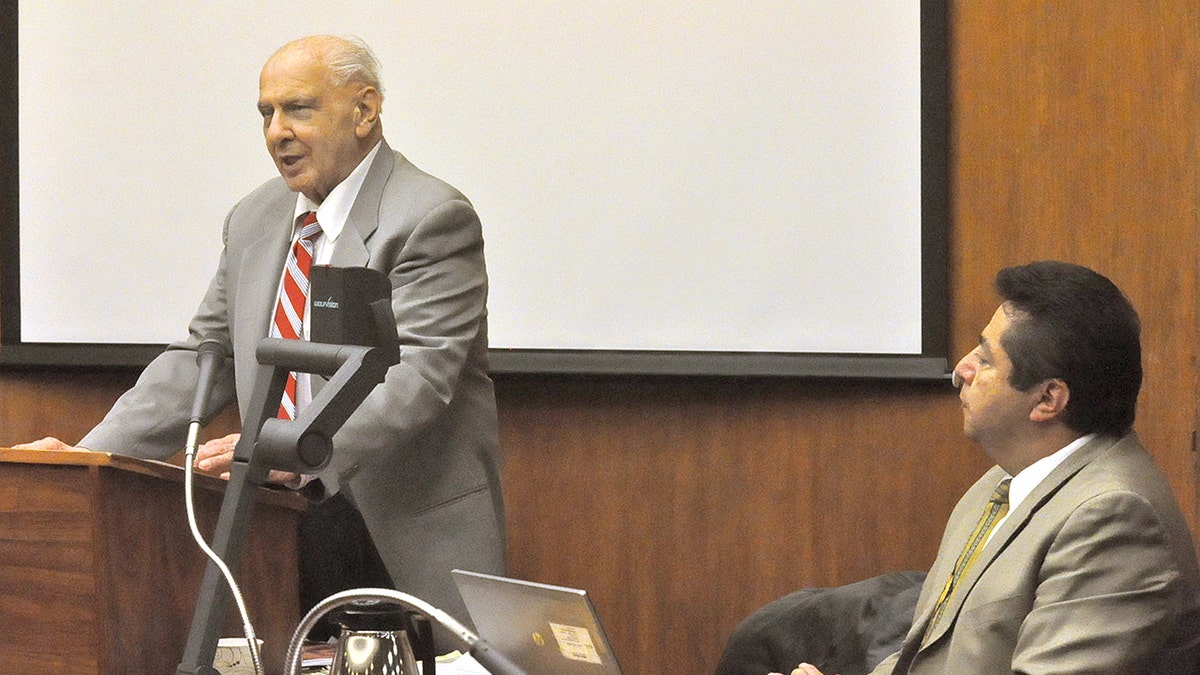 Joseph Naso testifying in court wearing a suit as a lawyer looks on.