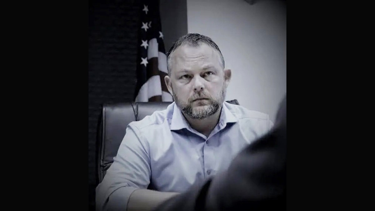 Ken Mains looking ahead at the camera with the American flag behind him.