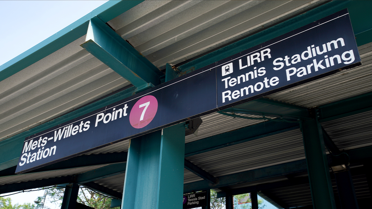 The Mets-Willets Point subway station signage hangs from green-painted steel beams