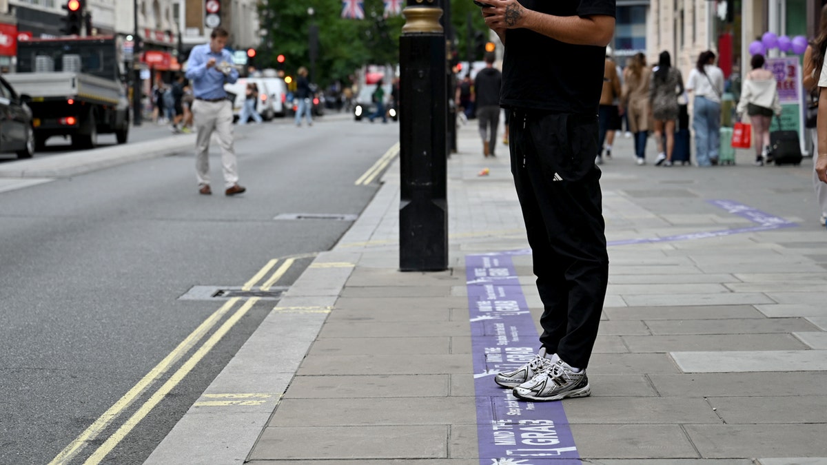 man on phone on oxford street in london standing on Mind the Grab campaign sign