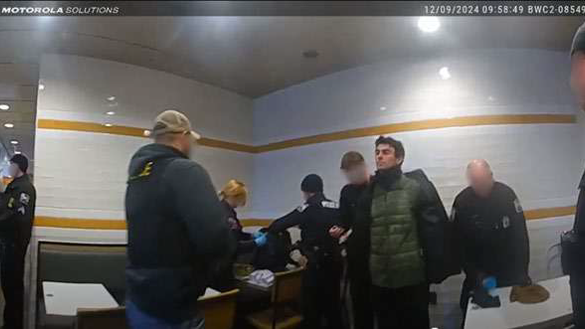 A man identified as Luigi Mangione is in handcuffs as police search his bag and other belongings