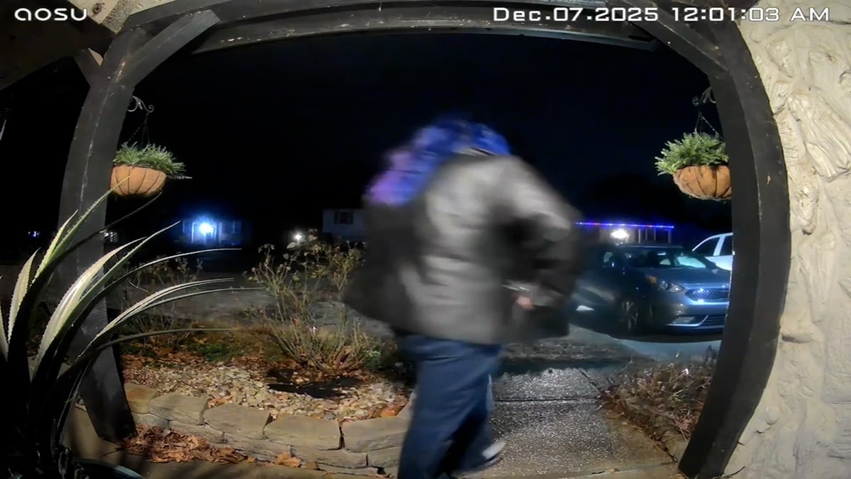 Woman with purple hair and leather jacket leaves home entrance.