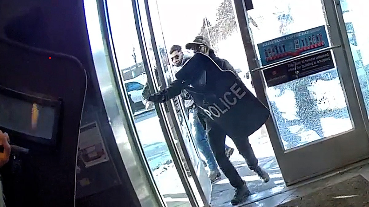 Police with shields opens doors entering building.