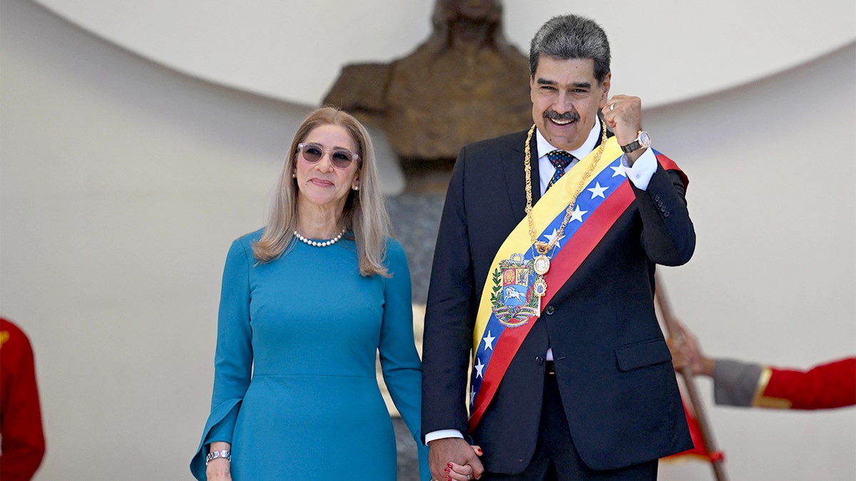 Venezuelan leader raises a hand while walking with his spouse.
