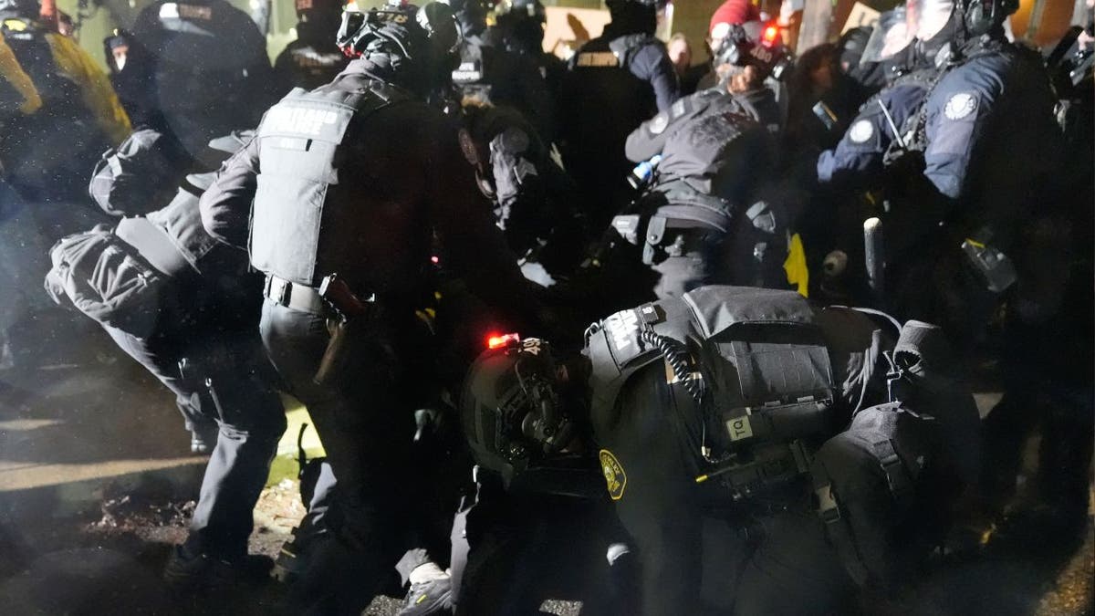 Portland police officers in riot gear detain protesters during a nighttime ICE protest.