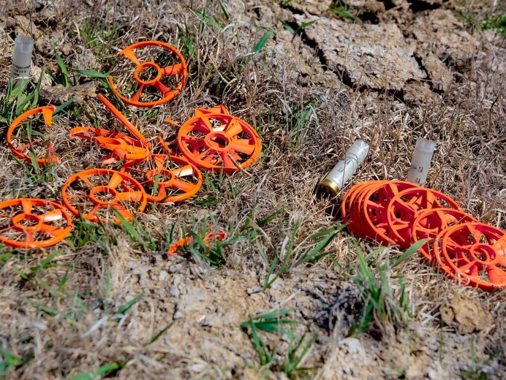 A pile of Caldwell ClayCopter clays laying in the dirt next to two spent shotgun hulls.